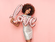 © Oleg Gekman - A beautiful young African-American woman with a balloon in the shape of the inscription love on a pink background. Woman on Valentine's Day. Symbol of love