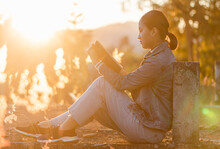 Beautiful Young Girl Sitting And Reading A Book Sunset Background. Warm Sunset Colors.