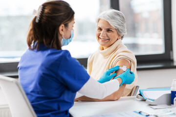 medicine, health and vaccination concept - doctor or nurse applying medical patch to vaccinated seni