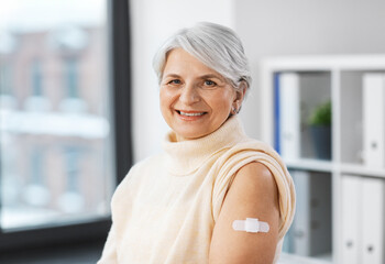 Poster - medicine, health and vaccination concept - happy smiling vaccinated senior woman with medical patch on arm at hospital