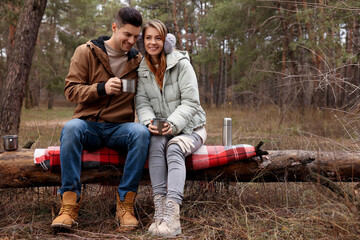 Wall Mural - Happy couple with hot drinks spending time together in forest