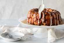 Apple Cinnamon Monkey Bread On A Pedestal Stand With Icing Being Drizzled On Top
