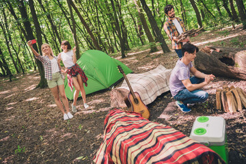 Poster - Portrait of attractive cheerful four people resting in wild park on fresh air having fun setting fire taking selfie showing v-sign outdoors