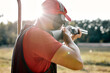 © Roman - Rear view on handsome Male in cap and headset shooting at target on an outdoor shooting range at sunny day, training alone, confident and skilled, experienced. Shooting and Weapons. view from back.