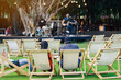 Back view of Asian young couple sit to relax on white deck chairs with tables for dinner in lawn is surrounded by shady green grass with blurred image of musical performance on stage in background.