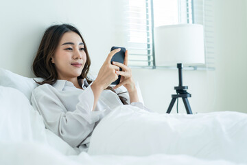 Wall Mural - Asian attractive woman use mobile phone chat on bed at home in morning. 