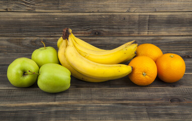 Green apples, bananas, oranges on wooden background.