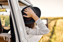 On The Way To Unknown Places. Rear View On Young Woman Leaning Out The Vans Window, Enjoying The Car Travel. Attractive Caucasian Female In Casual Wear, Smiling, Have Rest In Nature. Travel