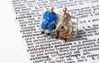 A conceptual image with miniature figures of an old aged elderly couple sitting next to the phrase Retirement Pension on the page of a dictionary