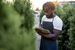 © Roman - Agriculture man holding notebook,researcher is checking the progress and growth of plants. Black guy taking notes on the report paper in agriculture Field. Research and Education Concepts.