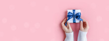 Banner Of Female Hands In Sweater Holding Gift In White Wrapping Paper On Pink Background. St. Valentines Day, Love, Tenderness, Friendship, Birthday, Christmas Concept. Festive Wallpaper. Color 2022