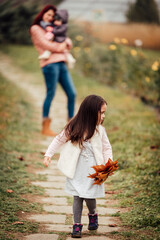 Wall Mural - Child running in the park, mother and sister in the background