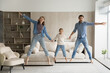 © fizkes - Emotional joyful young couple parents holding hands of laughing adorable little child daughter, looking at camera jumping barefoot in modern living room, celebrating moving into own apartment.