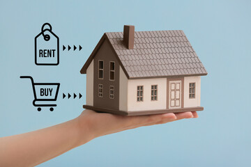 Poster - Female hand with figure of house on blue background. Concept of choice between renting and buying