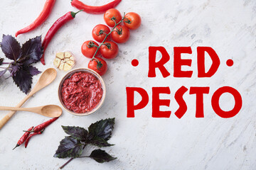 Bowl of tasty red pesto sauce and ingredients on light background