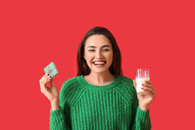 Pretty Young Woman With Gingerbread Cookie And Glass Of Milk On Red Background