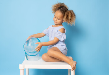 Cute little girl in summer clothing sitting over a table playing over blue background.