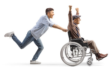 Wall Mural - Full length profile shot of a young man running and pushing a happy elderly man in a wheelchair