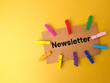 Colored wooden clips and brown card written with text Newsletter on yellow background.