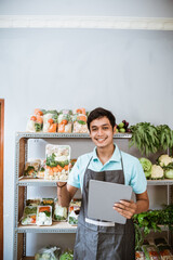 Wall Mural - Vegetable seller showing vegetables while holding a digital tablet