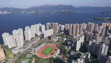 Football Field And Running Track Between The High Populated Skyscrapers Of Vista Paradiso While A Train Is Moving Over The Railway Track In Hongkong. Wide Panning Shot