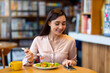 © Prostock-studio - Happy young arab woman texting on smartphone while eating salad in cafe, using an application to send an sms