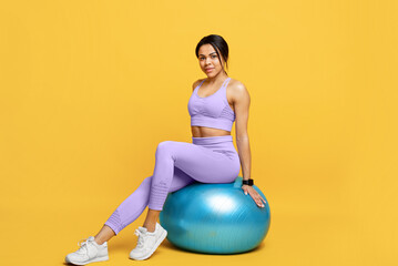 Wall Mural - Fitness workout concept. Happy slim african american lady sitting on fitball and smiling over yellow background