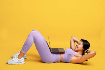Wall Mural - Online gym. Fit african american lady doing abs exercise sit-ups, training with laptop, exercising on yellow background