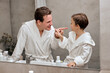 © Roman - caucasian parent man with child boy in white bathrobes having morning routine in hotel bathroom, standing near the mirror. dad with son examining teeth. Family vacation, healthcare concept.