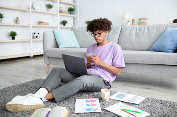 Poster - Full length of focused black teen guy using smartphone and laptop for online learning at home