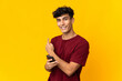 © luismolinero - Young Argentinian man isolated on yellow background using mobile phone and pointing back