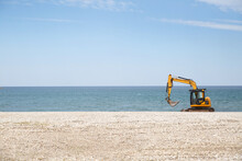 Yellow Excavator Works On The Beach Against The Background Of The Sea.