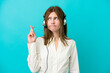 © luismolinero - Telemarketer English woman working with a headset isolated on blue background with fingers crossing and wishing the best