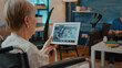 © DC Studio - Elder person in wheelchair holding tablet with online video call to chat with family in hospital. Retired adult with physical disability talking on teleconference for remote communication.