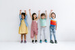 Group of Diverse Ethnicity Little kids raising hands up and smiling Isolated on gray background. Childhood, freedom, happiness, active lifestyle concept.