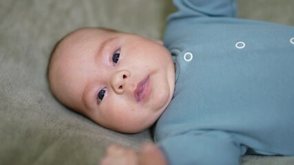 Wall Mural - Adorable sleepy infant boy resting on the bed. Sweet yawning infant child in blue shirt close up. Grey blanket background.