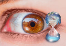 Global Warming Concept -  Close-up Shot Of The Eye Of A Young Girl With A Frightened Look - Planet Earth On Hourglass Is Slowly Melting