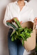 © Dina - woman in white shirt and jeans holding an eco jute reusable bag with bunch of green basil and lettuce. Grocery shopping for vegetables - healthy lifestyle
