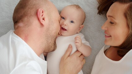 Wall Mural - Happy parents with his newborn baby, top view. Happy family. Healthy newborn baby with mom and dad. Close up Faces of the mother, father and infant baby. Cute Infant boy and parents.