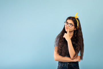 Wall Mural - Pensive Indian teen girl in casual wear looking at copy space over blue studio background