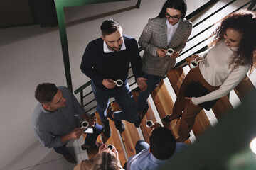 Poster - Group of coworkers talking during coffee break on stairs in office, above view