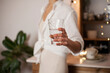 © Dina - Unrecognizable woman in white shirt holding a glass of water, standing in the kitchen with evening light. Healthy lifestyle - drinking enough water every day