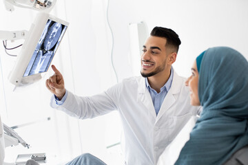 Wall Mural - Middle-Eastern Stomatologist Showing Teeth Xray Picture On Digital Monitor To Islamic Female