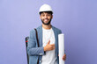 © luismolinero - Young architect Moroccan man with helmet and holding blueprints over isolated background giving a thumbs up gesture
