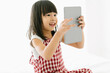 Excited little Asian girl using digital tablet while sitting on bed in bedroom. Happy preschool smart kid playing with tablet looking at screen watching cartoons online at home. Kid activity concept