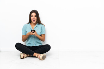 Wall Mural - Teenager girl sitting on the floor surprised and sending a message