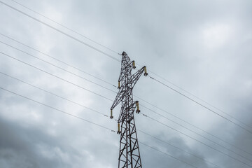 Tall tower of power lines on background of gray cloudy sky. High electric tower with wires against cloudy gray sky. Tower of electricity in overcast. Сloudscape with power lines against gray clouds.