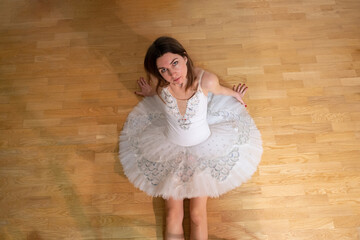 Ballerina in a white tutu on the floor looking up
