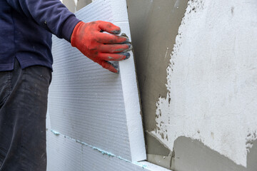 Construction worker installing styrofoam insulation sheets on house facade wall for thermal protection