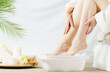 Closeup view of woman soaking her feet in dish with water and flowers on floor. Spa treatment